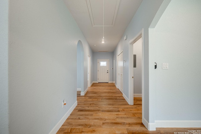 corridor with light wood-style floors, baseboards, and attic access