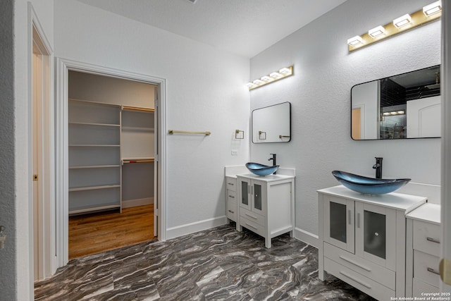 bathroom featuring a sink, a walk in closet, marble finish floor, and two vanities