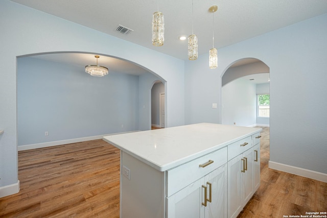 kitchen featuring light wood finished floors, arched walkways, decorative light fixtures, open floor plan, and visible vents