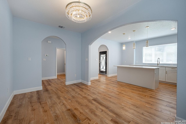 unfurnished living room featuring visible vents, arched walkways, light wood-style floors, and an inviting chandelier