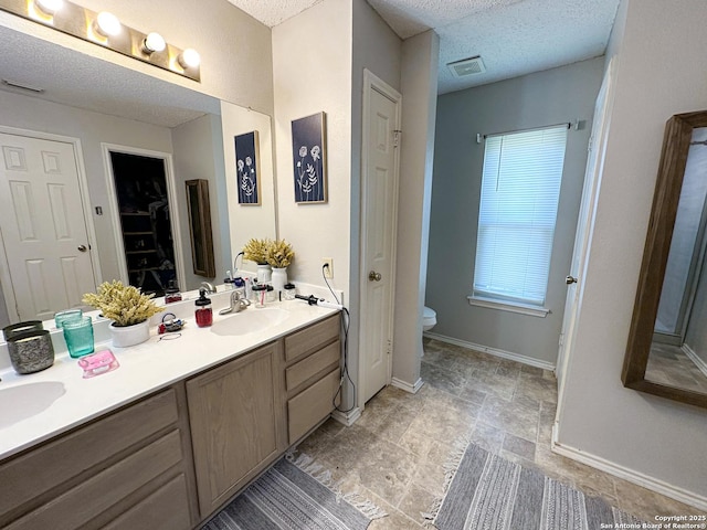 bathroom featuring a sink, toilet, double vanity, a textured ceiling, and visible vents