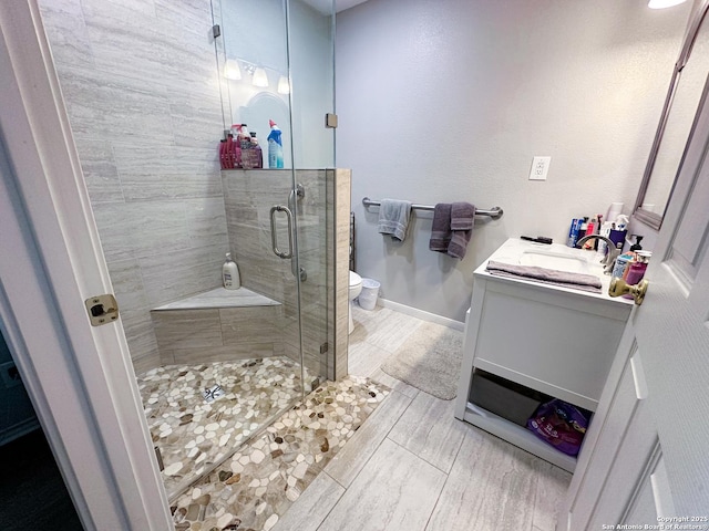 bathroom featuring toilet, baseboards, a shower stall, and vanity