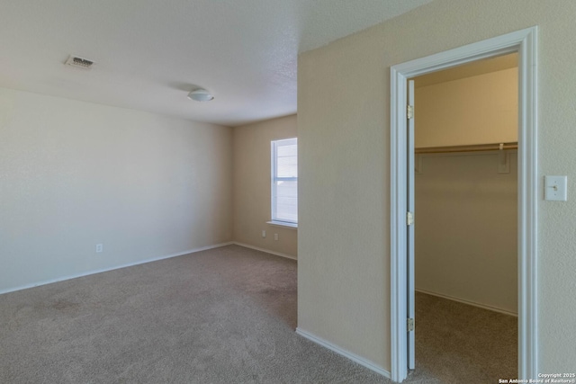 unfurnished bedroom with carpet floors, visible vents, a walk in closet, and a closet