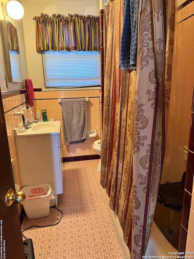 bathroom featuring vanity, a wainscoted wall, toilet, and tile walls