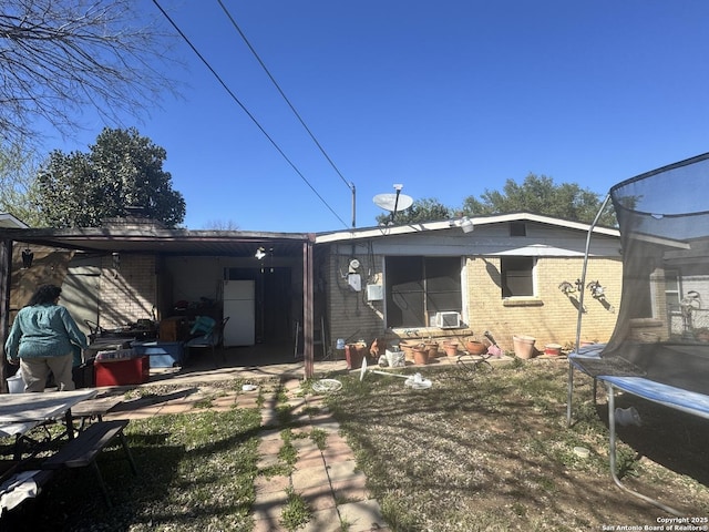 back of property featuring a trampoline, a patio, and brick siding