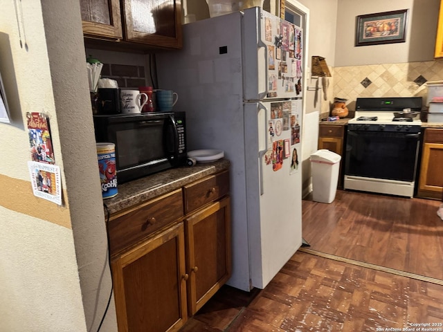 kitchen with brown cabinets, black microwave, gas stove, freestanding refrigerator, and backsplash