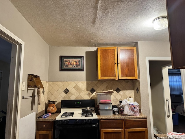 kitchen with a textured ceiling, decorative backsplash, brown cabinetry, and range with gas cooktop