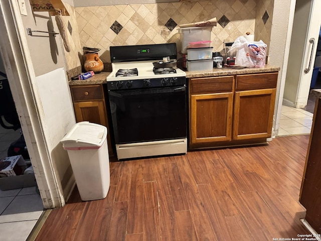 kitchen featuring wood finished floors, backsplash, and gas stove
