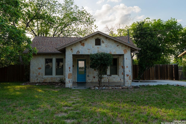 view of front facade featuring roof with shingles, fence, stone siding, and a front lawn