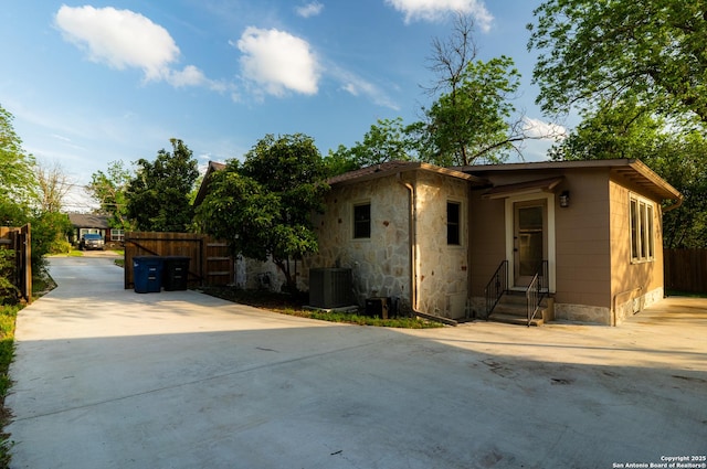 view of front facade featuring fence, concrete driveway, entry steps, and central AC