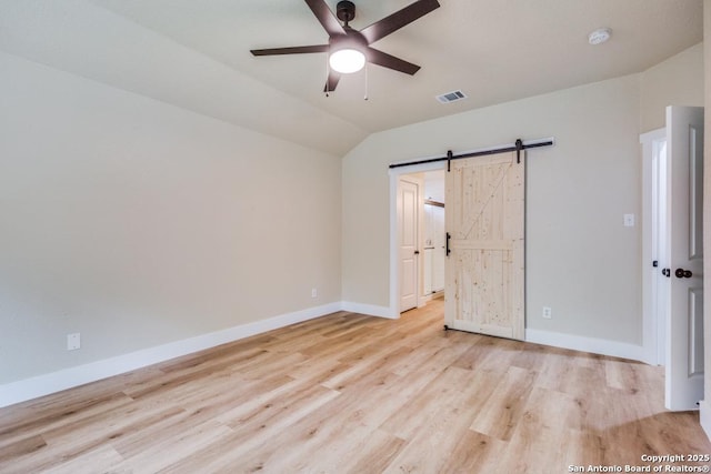 unfurnished bedroom with visible vents, vaulted ceiling, a barn door, baseboards, and light wood finished floors