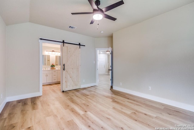 unfurnished bedroom featuring baseboards, light wood finished floors, a barn door, and visible vents