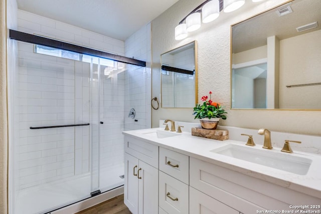 full bath with a sink, a shower stall, double vanity, and visible vents