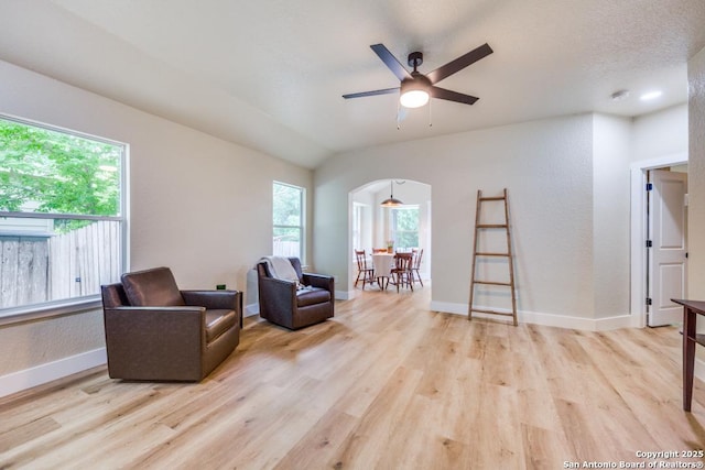 living area with arched walkways, baseboards, a ceiling fan, and light wood-style flooring