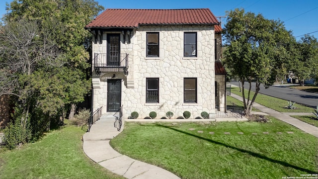 mediterranean / spanish-style home featuring a tiled roof, a front lawn, and stone siding