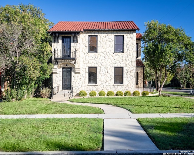 mediterranean / spanish house featuring a front lawn, a balcony, and stone siding
