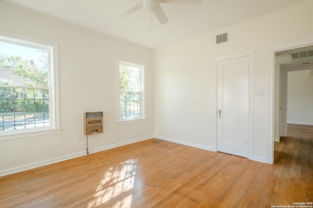 empty room featuring heating unit, a ceiling fan, light wood-style flooring, and a wealth of natural light