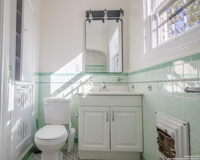 half bath with tile walls, wainscoting, tile patterned floors, vanity, and toilet