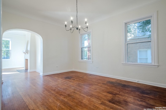 unfurnished room with an inviting chandelier, arched walkways, ornamental molding, and dark wood-type flooring