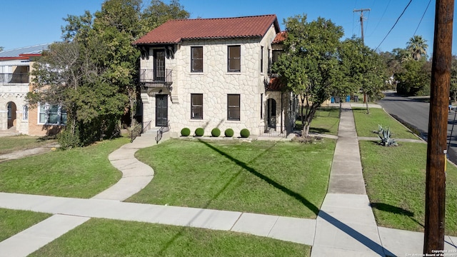 mediterranean / spanish home featuring a tiled roof, a balcony, stone siding, and a front lawn