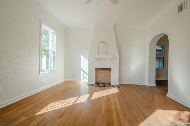 unfurnished living room with a fireplace, arched walkways, a ceiling fan, wood finished floors, and visible vents