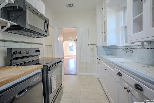 kitchen featuring white cabinets, an inviting chandelier, visible vents, glass insert cabinets, and black appliances