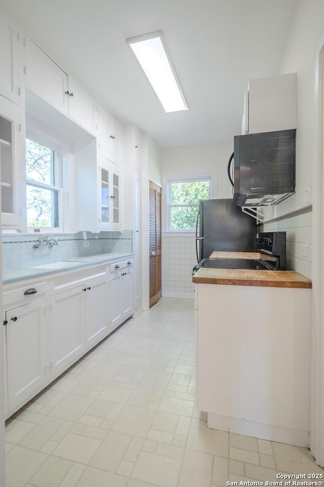 kitchen featuring black microwave, white cabinetry, tasteful backsplash, a sink, and range