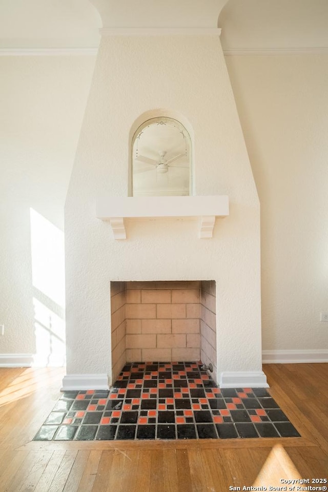 interior details featuring crown molding, baseboards, wood finished floors, and a fireplace with flush hearth