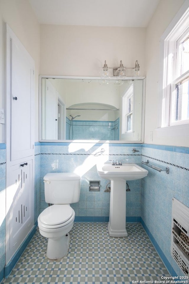 bathroom with heating unit, tile patterned floors, toilet, and tile walls