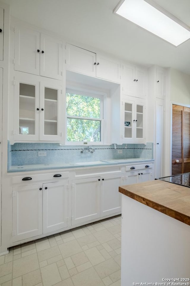 kitchen featuring decorative backsplash, wooden counters, a sink, white cabinets, and glass insert cabinets