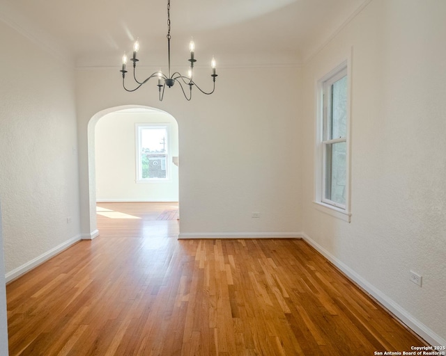 empty room with crown molding, arched walkways, baseboards, light wood finished floors, and a notable chandelier