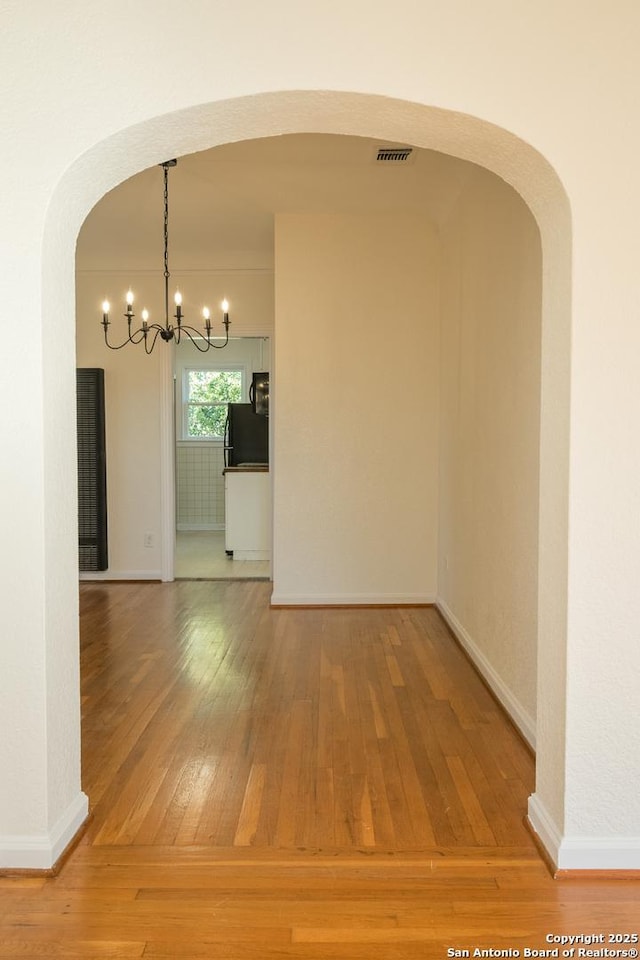 unfurnished dining area featuring an inviting chandelier, arched walkways, hardwood / wood-style floors, and visible vents