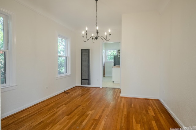 unfurnished dining area featuring a wealth of natural light, a notable chandelier, light wood-style flooring, and a heating unit