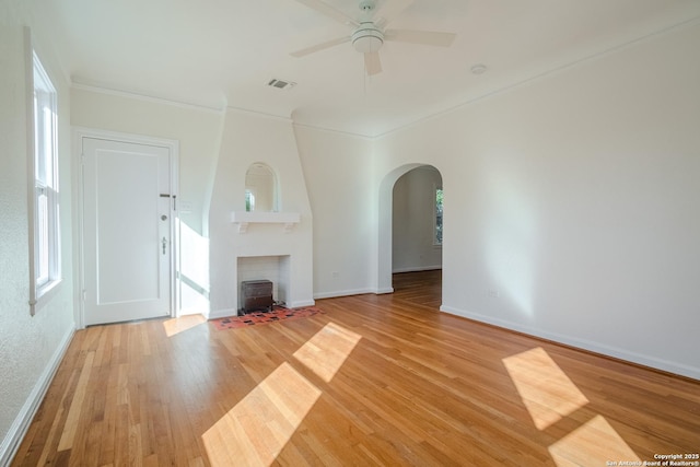 unfurnished living room with visible vents, a ceiling fan, crown molding, light wood-type flooring, and arched walkways