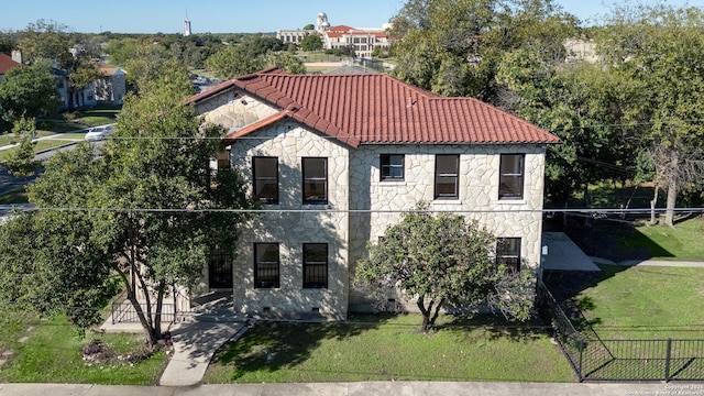mediterranean / spanish-style house featuring fence, a tile roof, stone siding, and a front lawn