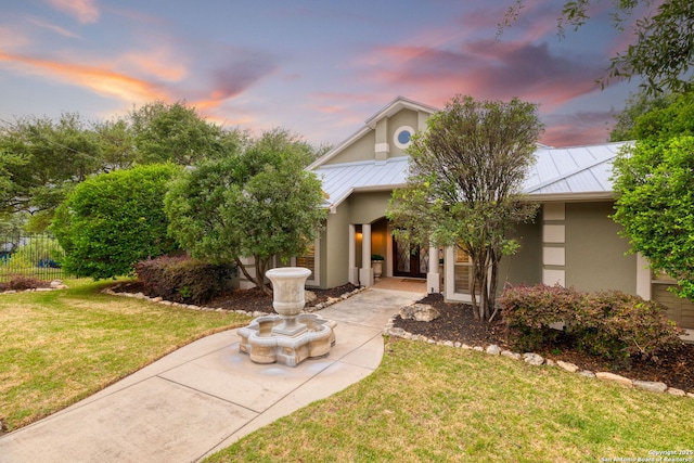view of front of property with a standing seam roof, metal roof, a lawn, fence, and stucco siding