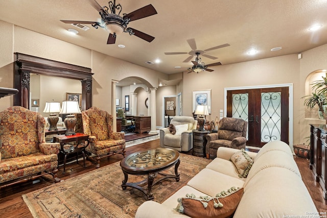 living area featuring arched walkways, wood-type flooring, a ceiling fan, and ornate columns