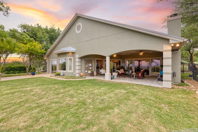 back of house at dusk with an outdoor living space, a chimney, a patio area, fence, and a yard