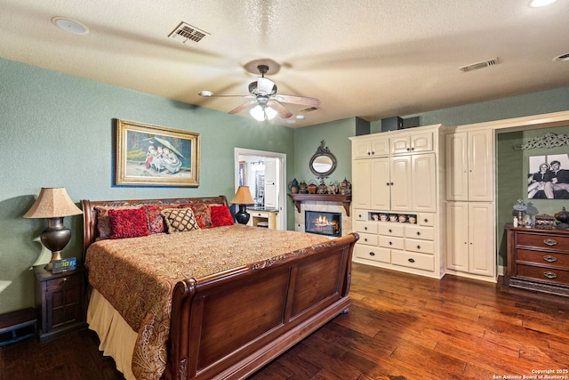 bedroom featuring a textured wall, a fireplace, dark wood-style flooring, and visible vents