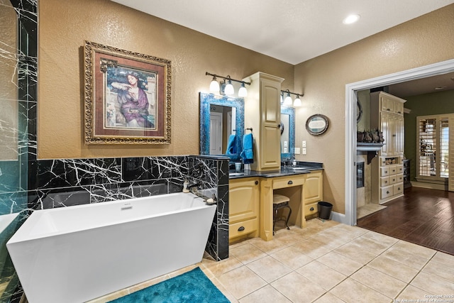 bathroom with a textured wall, a soaking tub, tile patterned floors, and vanity