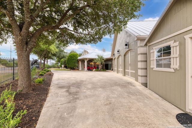 view of side of home featuring fence, concrete driveway, and metal roof