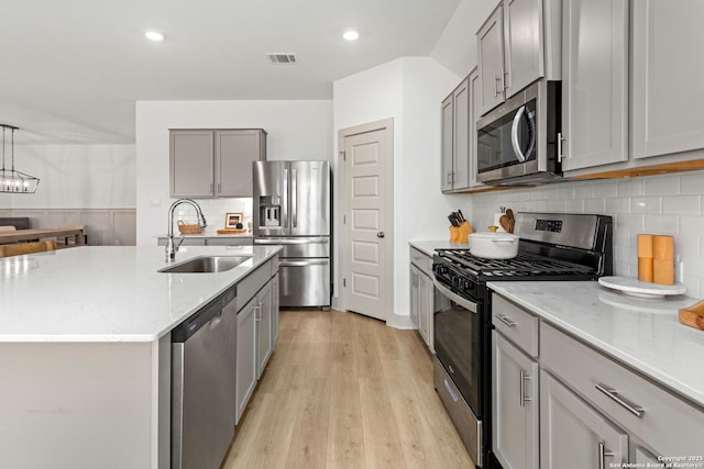 kitchen with visible vents, gray cabinets, light stone counters, a sink, and appliances with stainless steel finishes