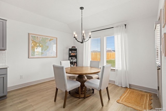 dining space featuring baseboards, a notable chandelier, vaulted ceiling, and light wood-style floors