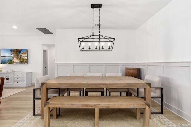 dining area with a wainscoted wall, visible vents, an inviting chandelier, and light wood-type flooring