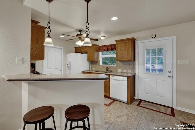 kitchen featuring a breakfast bar area, a ceiling fan, a sink, white appliances, and backsplash