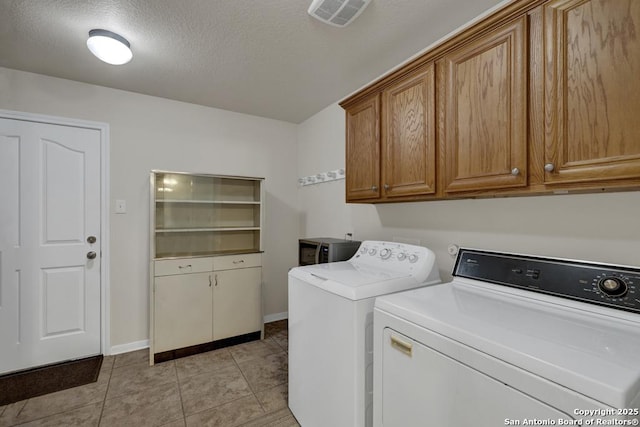 laundry room featuring cabinet space, a textured ceiling, light tile patterned flooring, visible vents, and separate washer and dryer