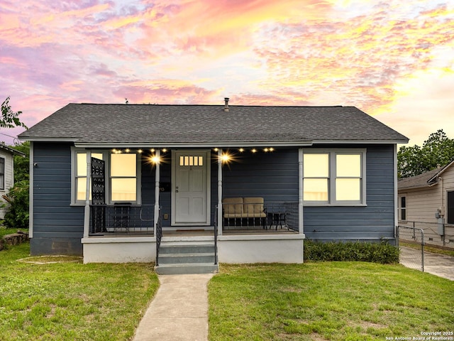 bungalow with a yard, a shingled roof, a porch, and fence