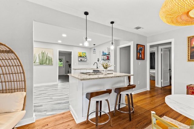 kitchen featuring baseboards, light wood-style flooring, visible vents, and a sink
