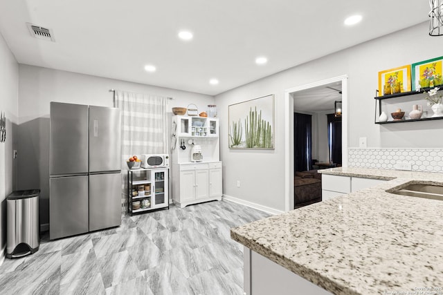 kitchen featuring freestanding refrigerator, open shelves, visible vents, backsplash, and light stone countertops