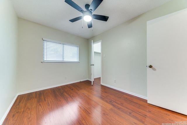 unfurnished bedroom featuring baseboards, a spacious closet, ceiling fan, and wood finished floors